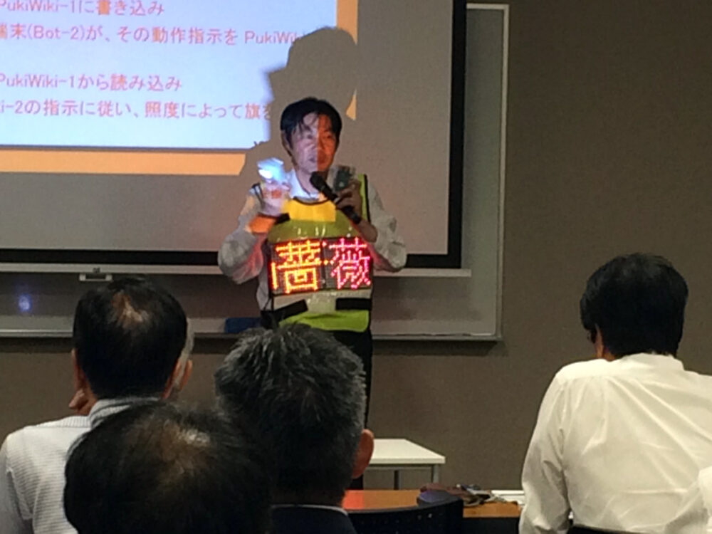 福山市モノづくりセミナー交流会「モノづくり大学IoTセミナー」にて、自作のTwitter（現：X）のツイートを表示する「着る電光掲示板」を着用して講演中の山之上先生