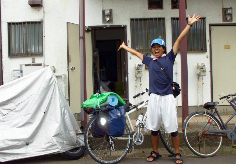 大学生の頃、自転車で四国を一周して帰宅したときの永嶋さん。自転車を傍らに大きく手を広げている