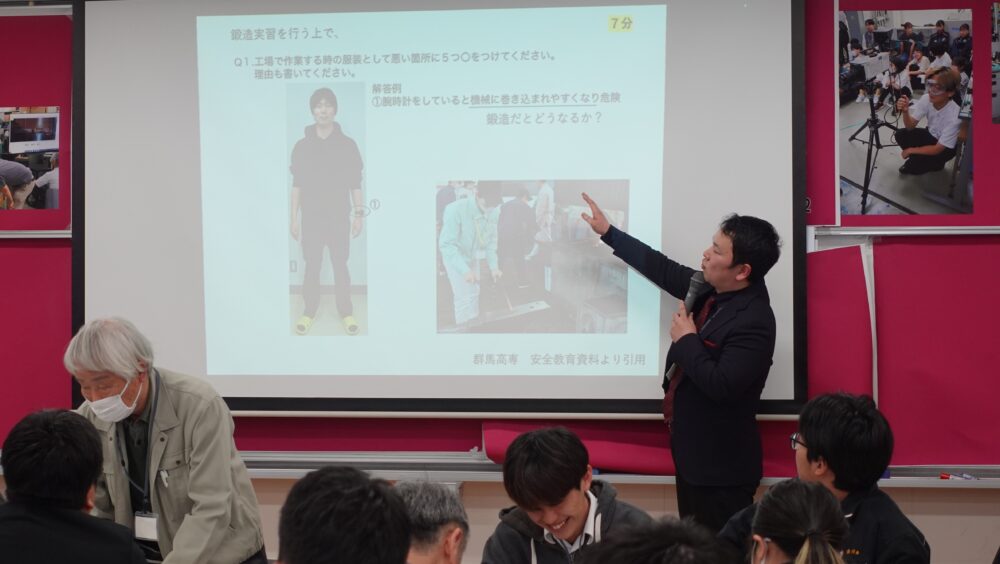 マテコンの司会・進行を務める久留米高専の佐々木先生が、安全講習のグループワークでのトークテーマについて説明中。スライドにある人物から、鍛造実習を行う服装として適切でない箇所を5つ見つけるというテーマでした