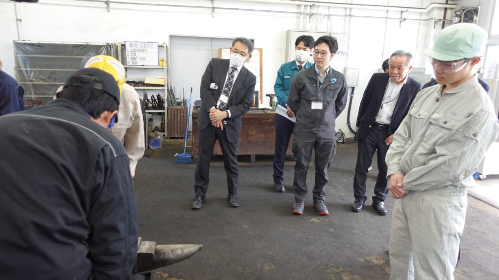 斜めになりながら学生による鍛造実習を見学する高専教員、企業・団体のみなさん