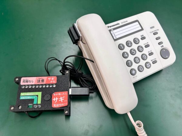 DCON本選時のFraudShield AI。固定電話にマイクやセンサーを取り付けて通話音声を拾い、音声とライトで詐欺の可能性推移をお知らせします。