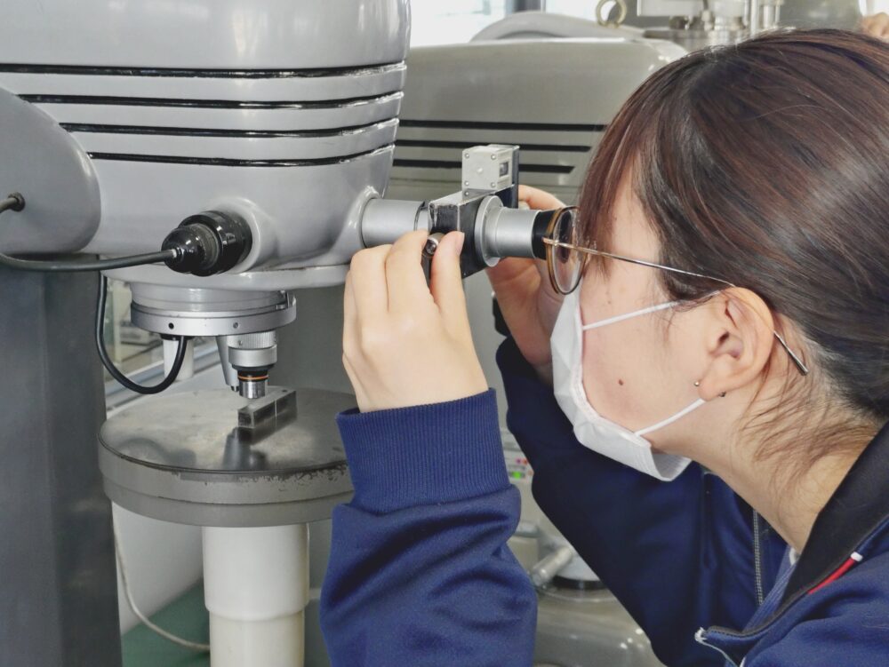 ビッカース硬さ試験の様子。正四角錐のダイヤモンド圧子を試験片に一定時間押し込み、できたくぼみの対角線の長さを測る様子。