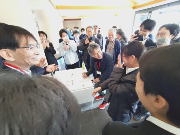 別会場でシャルピー衝撃試験を見ていた教員や企業・団体の方々から祝福を受ける奈良高専のみなさん。